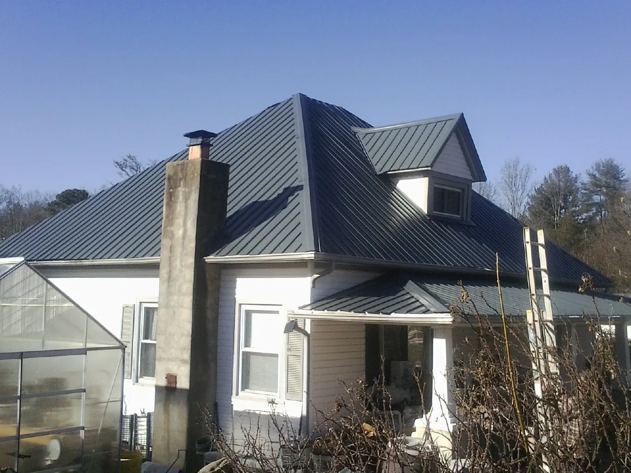 Dark blue standing seam metal roof on a white farmhouse with dormer — Slate & Tile Roof Repair by Roofing Brothers in Davenport Center