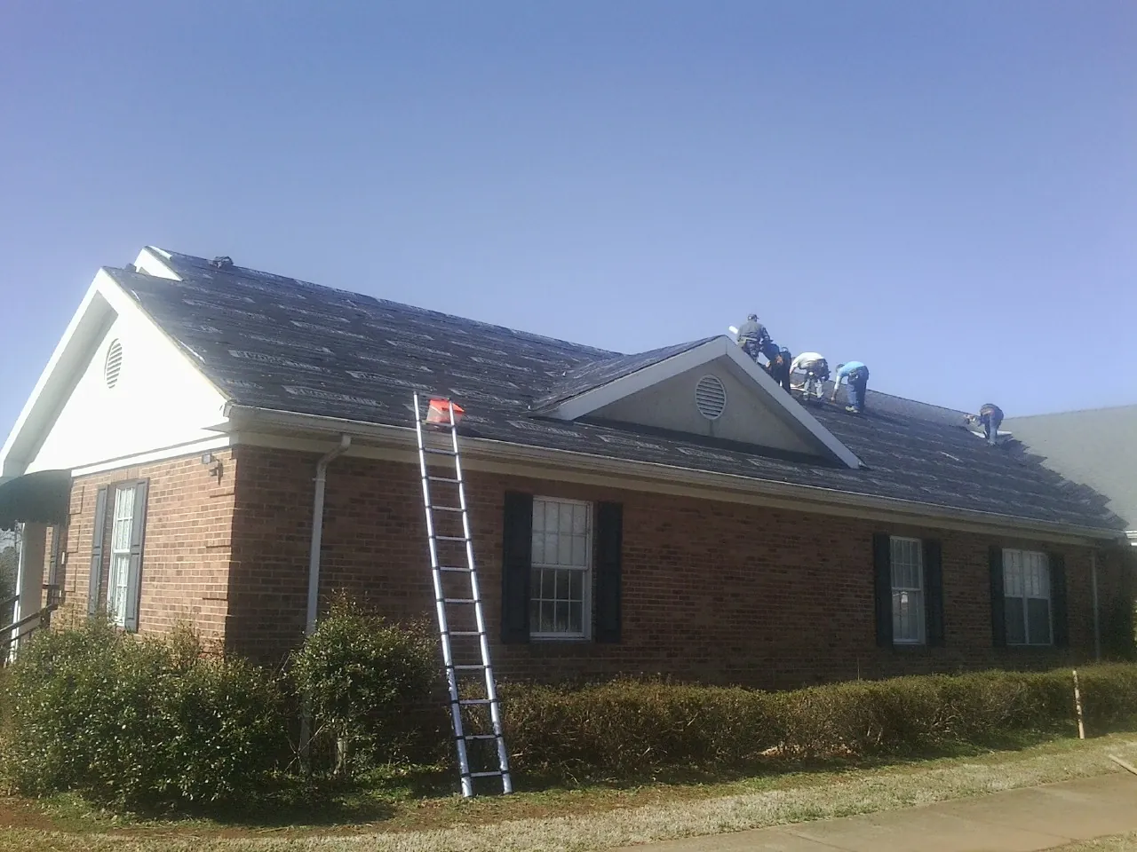 Crew tearing shingles off a brick ranch roof with a ladder set — Metal Roof Repair work by our crew in Davenport Center