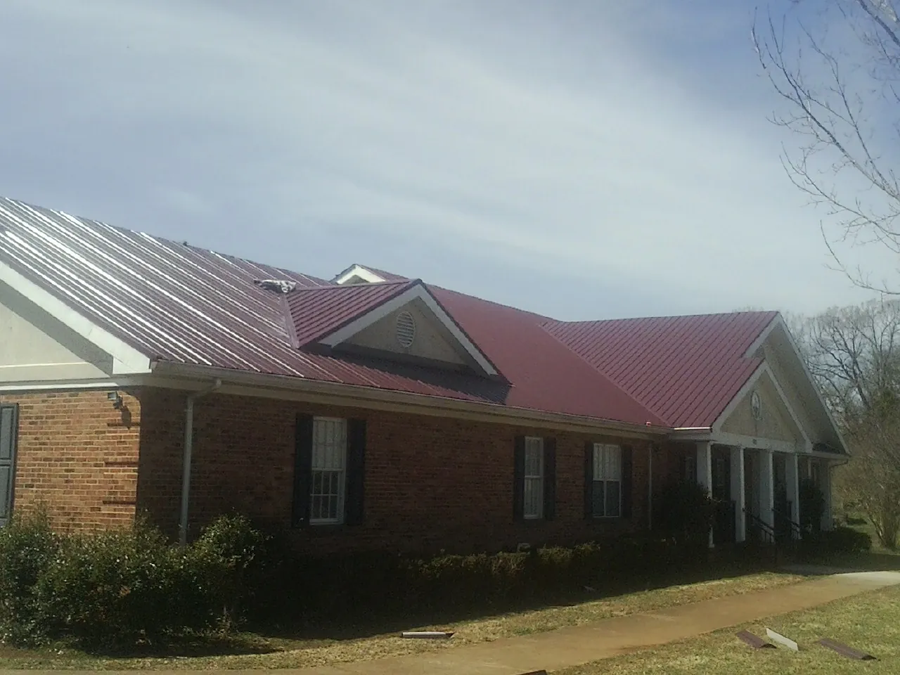 Red metal roof with gabled entries on a long brick building, from a Hail Damage Roof Repair job in Davenport Center