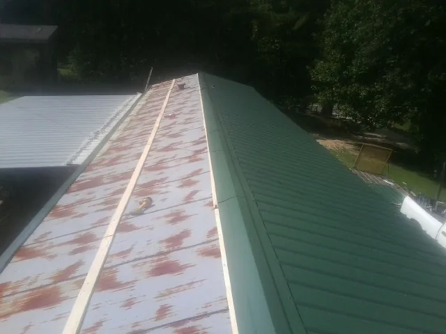 Old rusted panels beside newly installed green metal roofing — Wind Damage Roof Repair by Roofing Brothers in Davenport Center