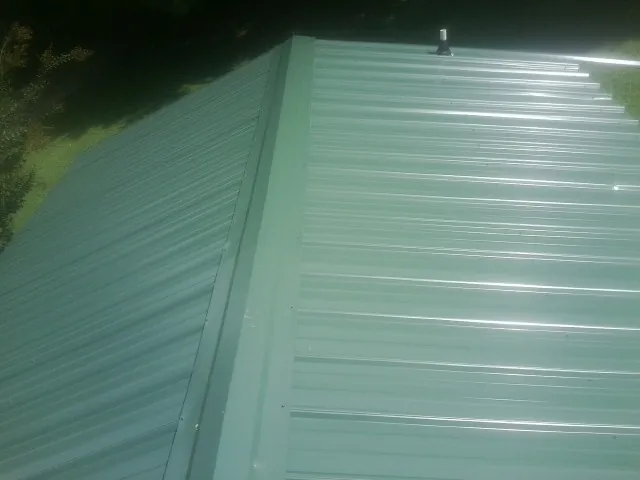 New green metal panels meeting at the ridge of a roof — Flat Roof Repair work by our crew in Davenport Center