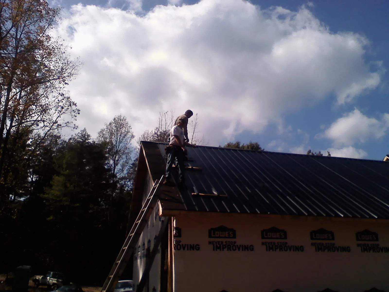 Roofer fastening dark metal panels high against a cloudy sky, from a Roof Inspection job in Davenport Center
