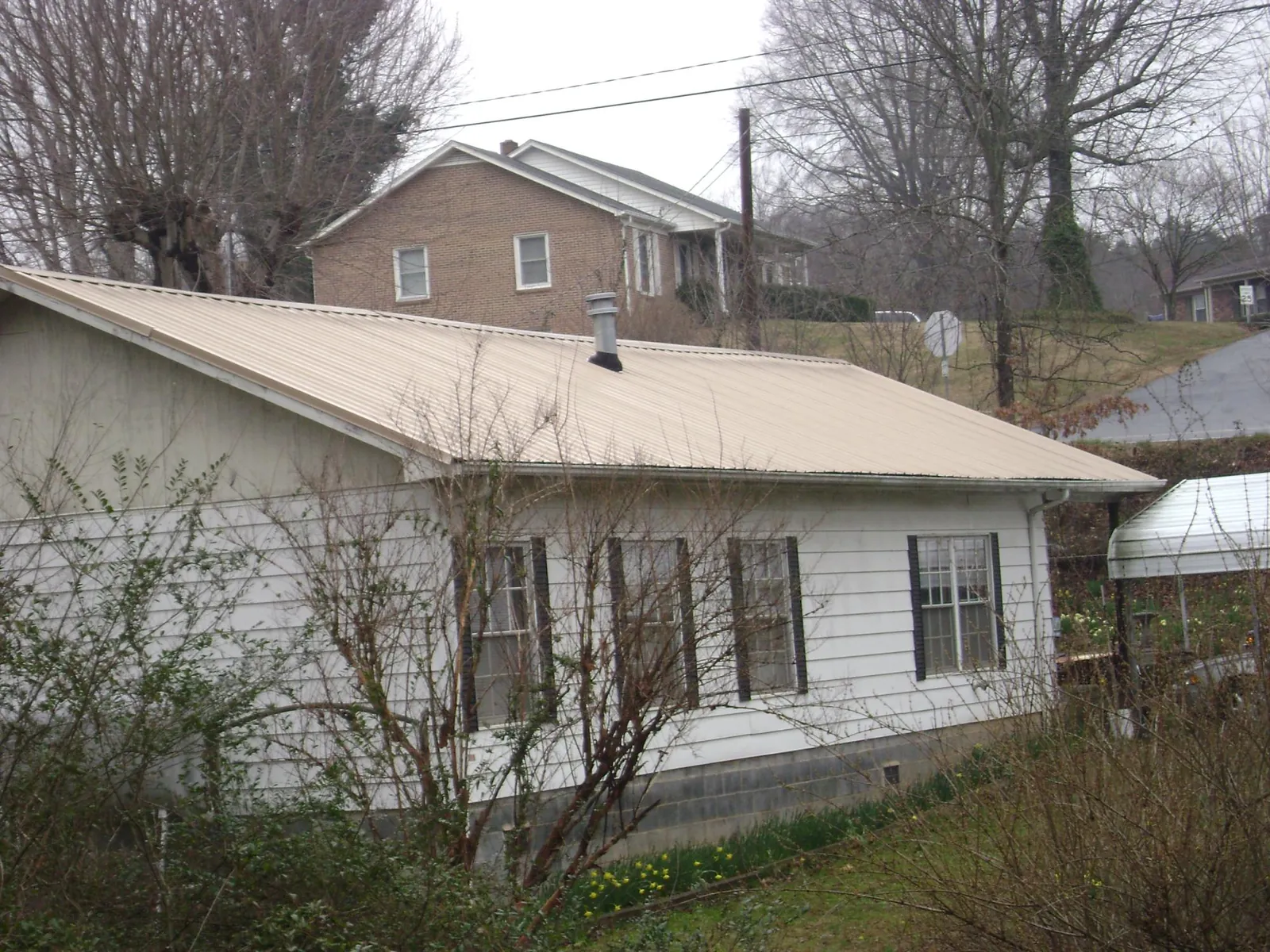 Tan metal roof on a white sided house set into a hillside — Commercial Roofing by Roofing Brothers in Davenport Center