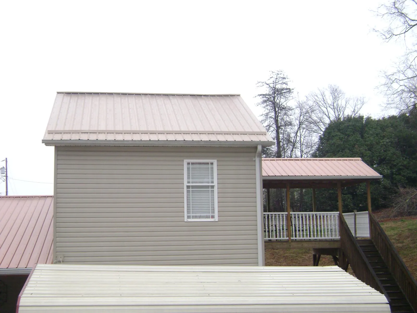 Tan metal roofs on a two story addition and attached porch, from a Roof Replacement job in Davenport Center